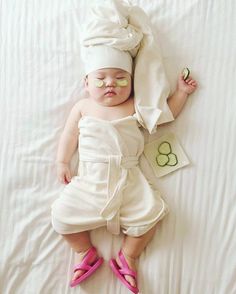 a baby in a white outfit laying on top of a bed