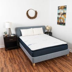 a bed in a room with wood flooring and white walls, next to a night stand