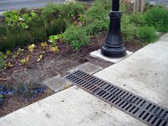 a black lamp post sitting on the side of a road next to a flower garden