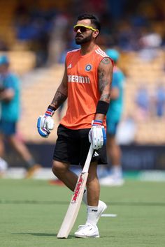 a man in an orange shirt and black shorts holding a cricket bat on a field