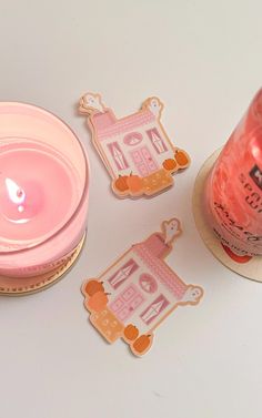 a candle and some stickers sitting on a table next to a cup with a pink liquid in it