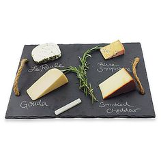 cheeses are arranged on a slate board with names written in cursive writing