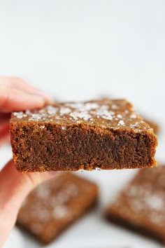 a hand holding up a piece of brownie with sugar on it's surface