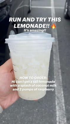 someone holding up a cup of lemonade in front of a parking lot full of cars