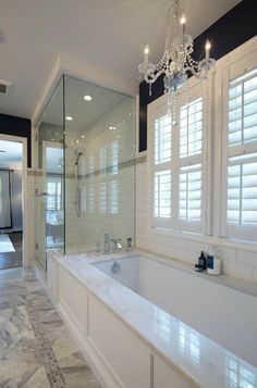 a large white bath tub sitting under a chandelier in a bathroom next to a walk in shower