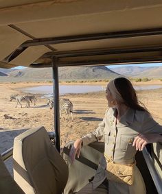 a woman sitting in the back of a safari vehicle looking at zebras and other animals