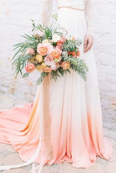 a woman holding a bouquet of flowers in her hand and wearing a dress with an ombreed skirt