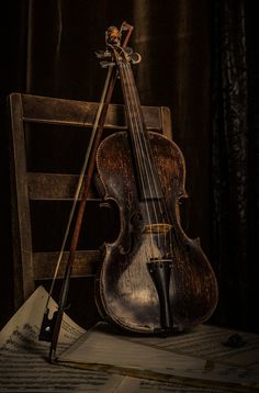 an old violin sitting on top of a wooden chair next to music sheets and pencils