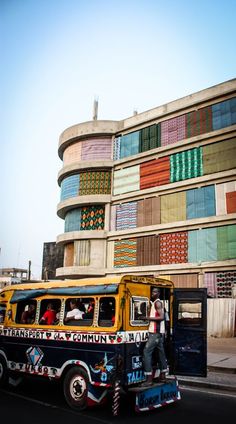 a colorful bus is driving down the street in front of a building with multicolored windows