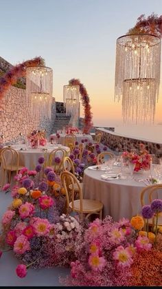 an outdoor dining area with flowers and chandeliers hanging from the ceiling at sunset