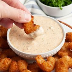 a person dipping something into a small bowl filled with ranch dip and tater tots