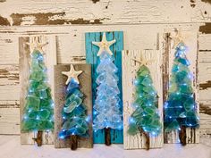 three small christmas trees are displayed in front of a white wooden wall with blue and green lights