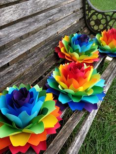 three colorful paper flowers sitting on top of a wooden bench in the grass next to a park bench