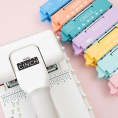 a bunch of different colored staplers sitting on top of a pink table next to each other