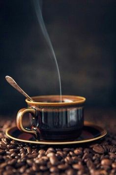 a coffee cup with steam rising out of it sitting on top of some coffee beans