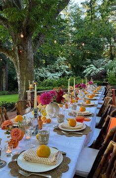 an outdoor dining table set with place settings and oranges on the plates, along with candles