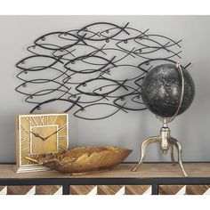 a metal wall clock sitting on top of a wooden table next to a bowl and an object