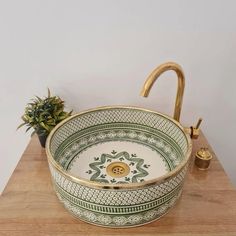 a green and white bowl sitting on top of a wooden table next to a potted plant