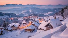 a snowy village with mountains in the background at sunset or dawn, surrounded by snow - covered trees