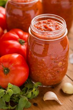 two jars filled with tomato sauce sitting on top of a table next to garlic and tomatoes