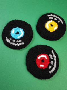 three black crocheted coasters with colorful eyeballs on them, sitting on a green surface