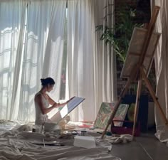 a woman sitting on the floor in front of an easel