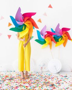 a woman in yellow jumpsuit standing next to two colorful pinwheels on top of confetti