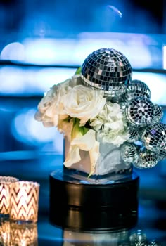 a table topped with a vase filled with white flowers and disco ball decorations on top of it