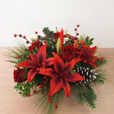 a bouquet of red flowers sitting on top of a wooden table next to pine cones