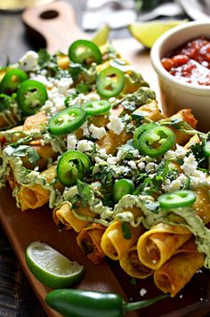 a wooden cutting board topped with tortilla shells covered in sauce and green peppers