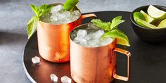 two copper mugs filled with ice and mint garnish on a black plate