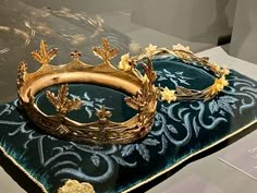 two gold crowns sitting on top of a blue cloth covered tablecloth in a glass case