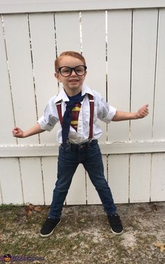 a young boy wearing glasses and suspenders standing in front of a white picket fence