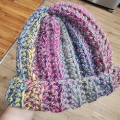 a hand holding a knitted hat on top of a wooden floor next to a laptop computer