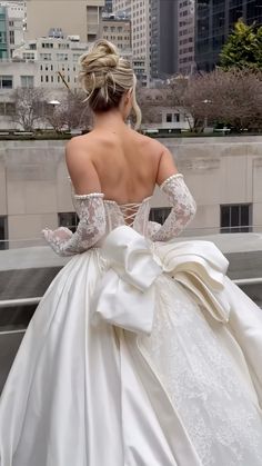 a woman in a white wedding dress looking out over the city from a balcony with her back to the camera