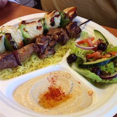 a white plate topped with meat and veggies on top of rice next to a salad