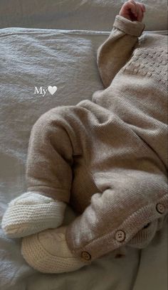 a baby laying on top of a bed wearing a sweater and slippers with the words my love written above it