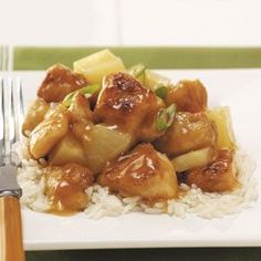 a white plate topped with chicken and pineapples on top of rice next to a fork