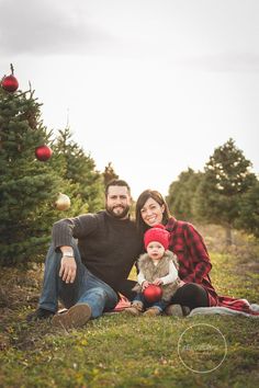 a man, woman and child sitting in front of a christmas tree at the park