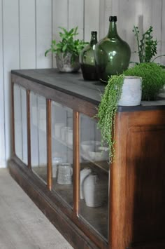 some green vases sitting on top of a wooden shelf next to other pots and plants