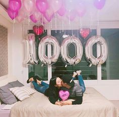 a woman laying on top of a bed with balloons hanging from the ceiling above her