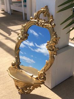 a gold mirror sitting on the ground next to a white pillar with a palm tree