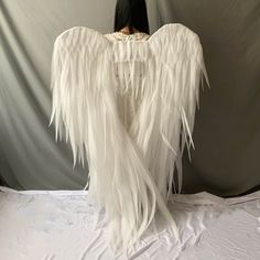 the back of a woman's body with white feathers on it, sitting on a bed