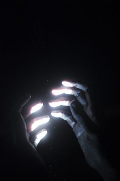 two hands holding something in the dark with light coming from them and their fingers pointing at it