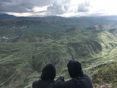 two people sitting on top of a hill looking at the mountains