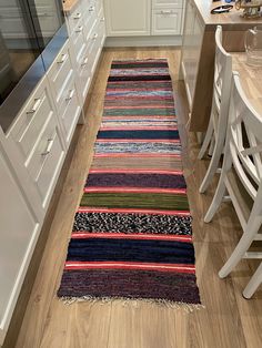 a kitchen with white cabinets and wooden flooring next to a rug on the floor