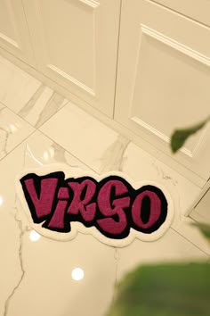 the word virgo written in red on a white tile floor next to a plant