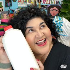 a woman with curly hair is holding a white bottle in front of her face and smiling at the camera