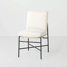 a white chair with black legs and a seat cushion on top of it, in front of a white wall