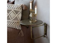 a small table with two candles on it next to a pillow and throw pillows in the corner